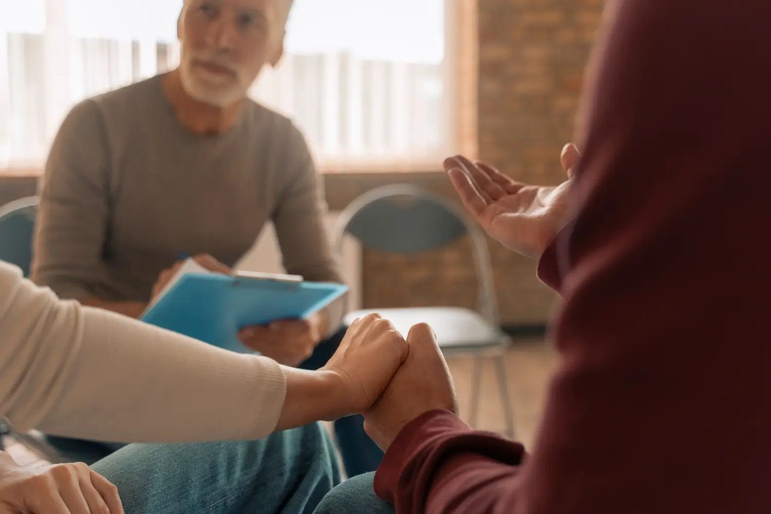 mental-health-providers Two people holding hands in front of a mental health provider in a therapy group setting, symbolizing support.